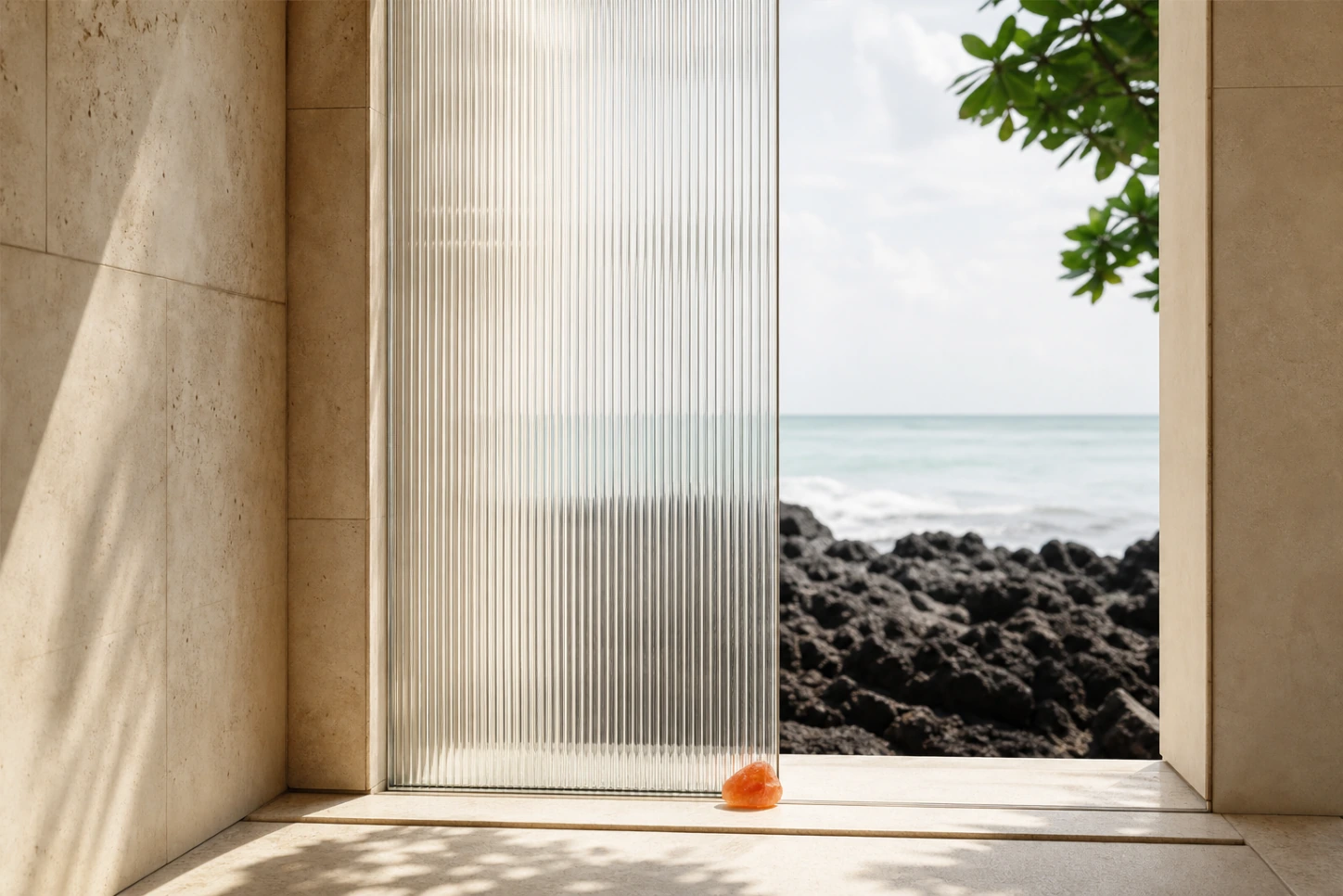 A clear fluted-glass threshold opening onto a volcanic Bali shoreline, marked by a restrained orange mineral.