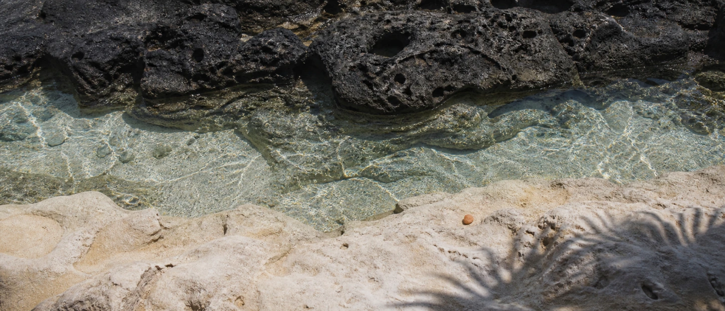 Clear tidal water passing between black volcanic rock and pale coastal limestone in Bali.