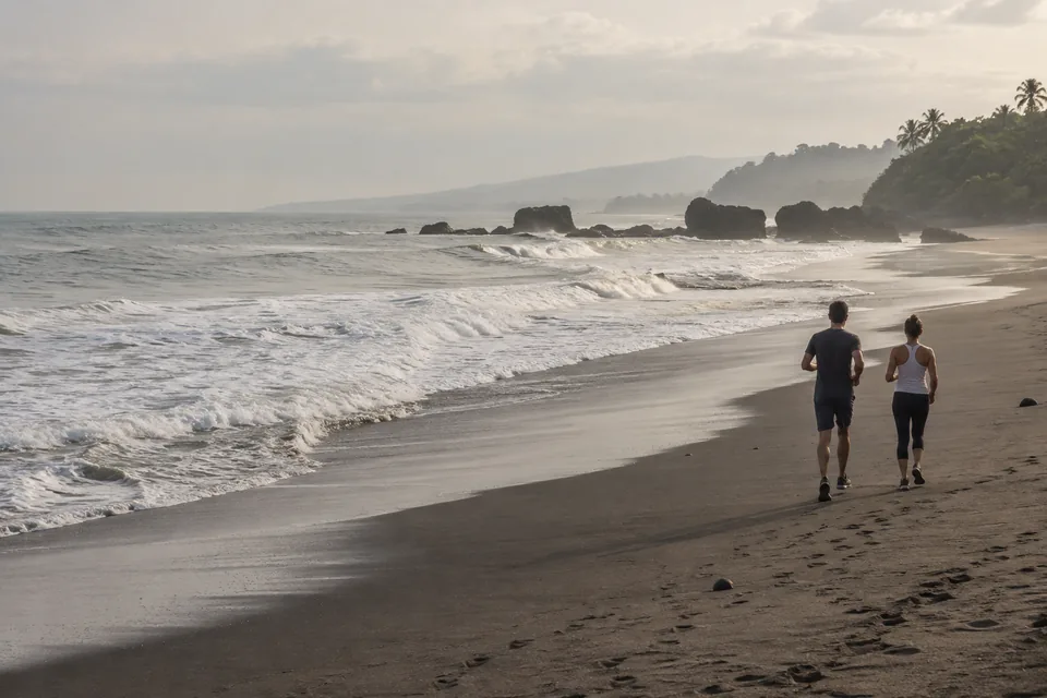 Two runners on a dark-sand beach at the water's edge.